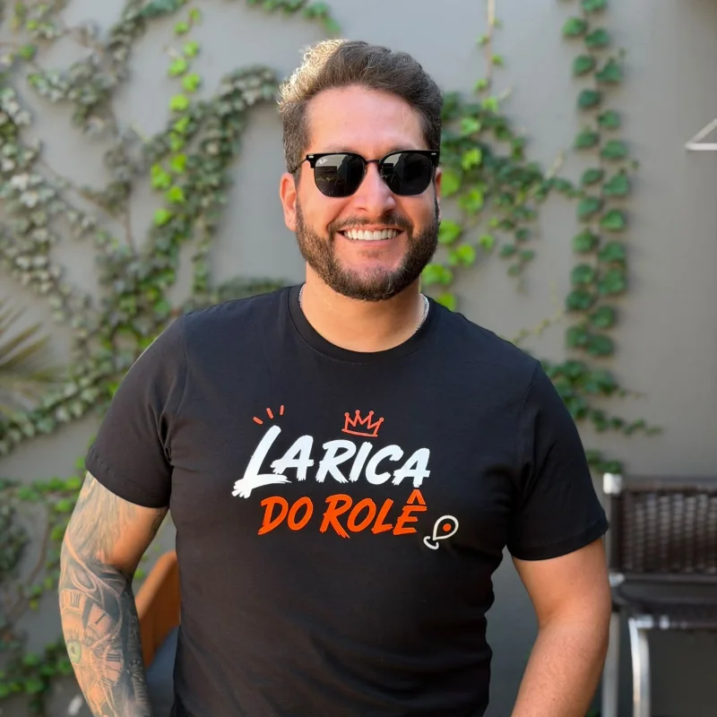 Rafael Brugim sorrindo, de óculos escuros e camiseta do Larica do Rolê